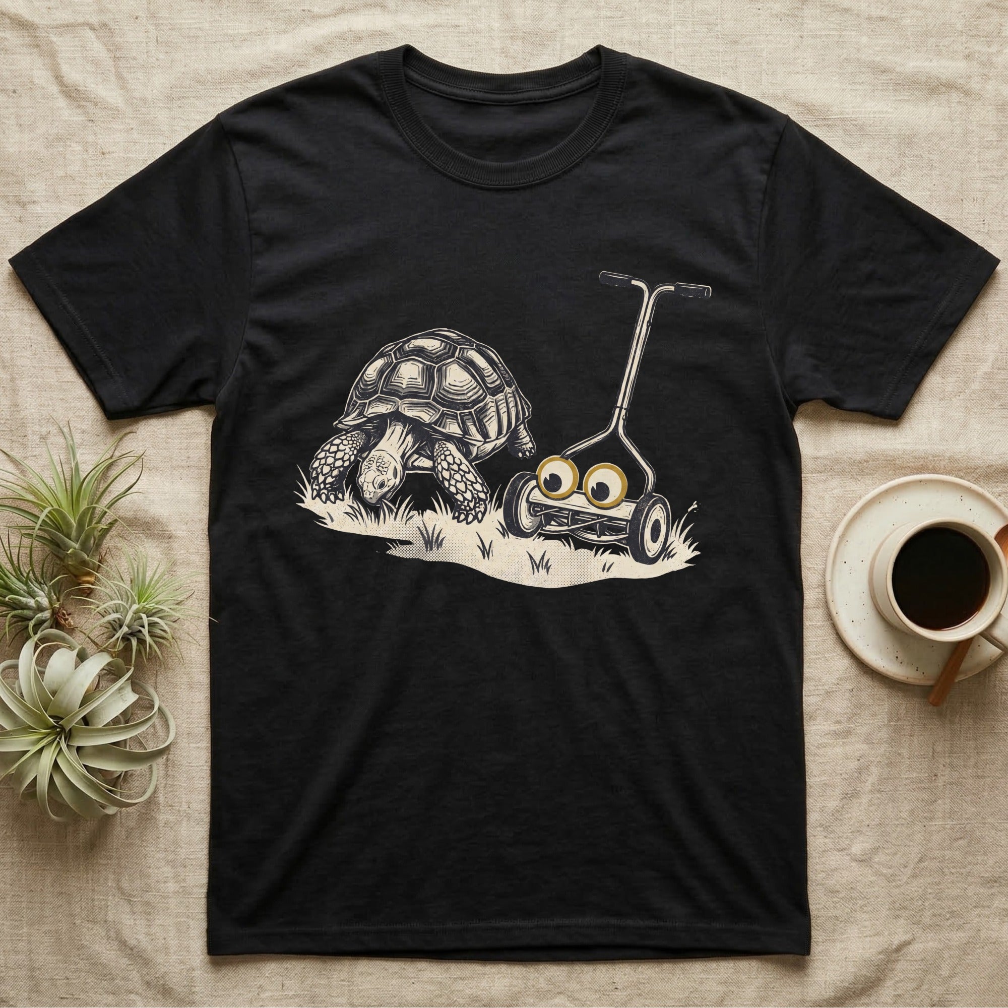 Tortoise Lawnmower Googly T-Shirt in Black — Linocut illustration of a sulcata tortoise grazing beside a push mower wearing oversized googly eyes.