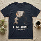 Deadpan photographic mugshot of a gargoyle gecko reaching toward the camera above the distressed text I Live Alone, it's a policy. — shown on a Navy tee.