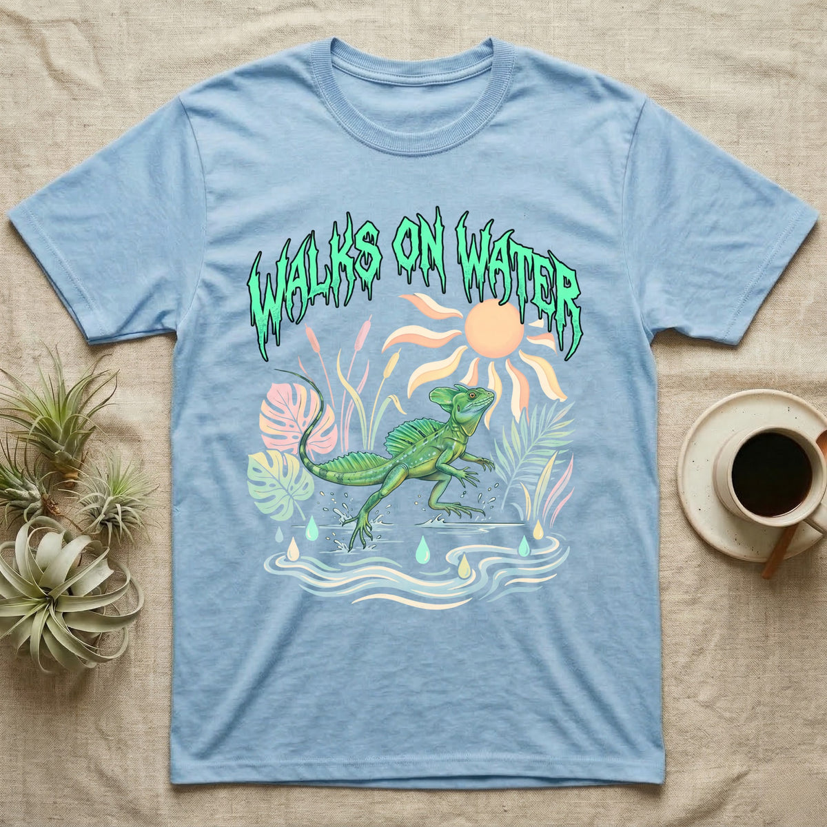 Green Basilisk Feral T-Shirt in Light Blue — Green plumed basilisk sprinting across water below a dripping aqua-green metal "Walks On Water" wordmark