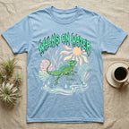 Green Basilisk Feral T-Shirt in Light Blue — Green plumed basilisk sprinting across water below a dripping aqua-green metal "Walks On Water" wordmark