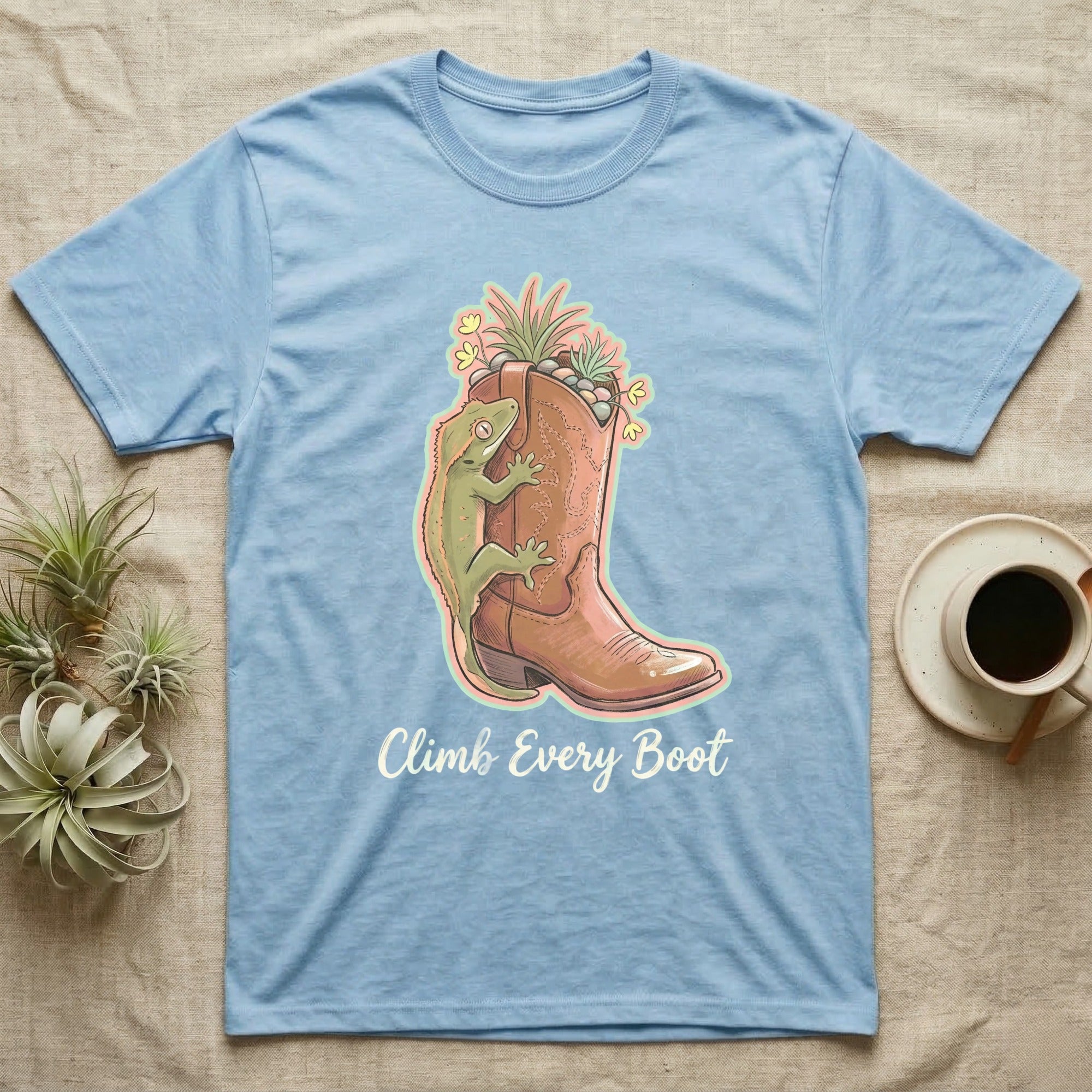 Light blue t-shirt with cowboy boot, gecko, and plants design, "Climb Every Boot" text.