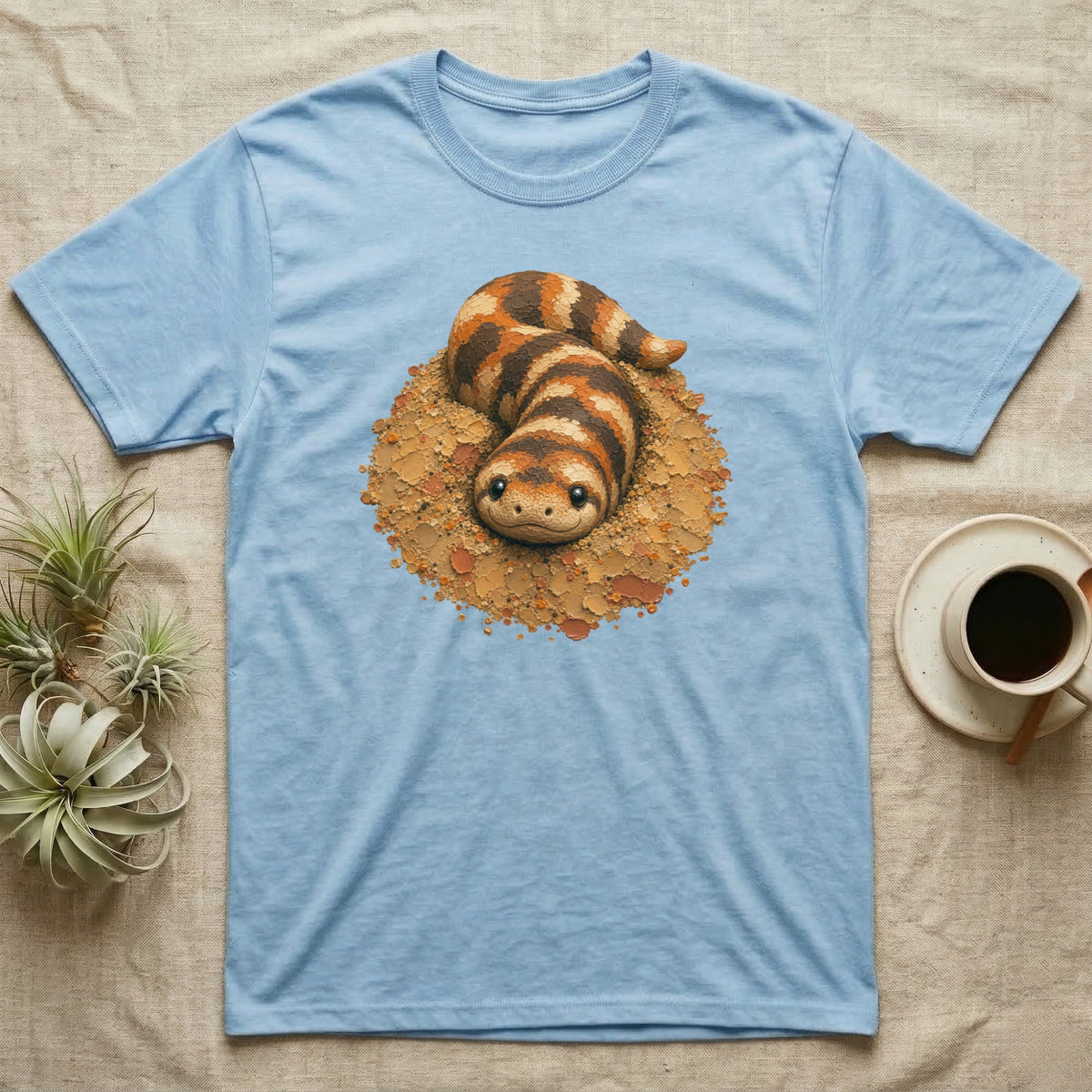 Light blue t-shirt with a cartoon sand lizard peeking from dirt.