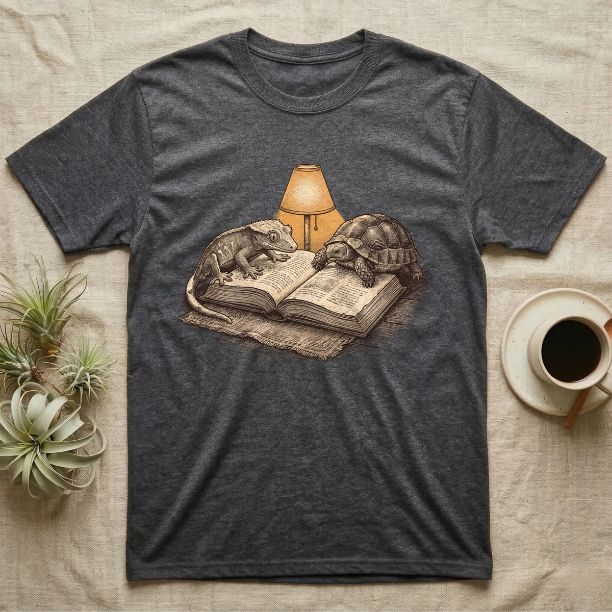 Cold-Blooded Book Club T-Shirt in Dark Heather — Engraved cozy illustration of a gecko and a tortoise sharing an open book under a glowing reading lamp.