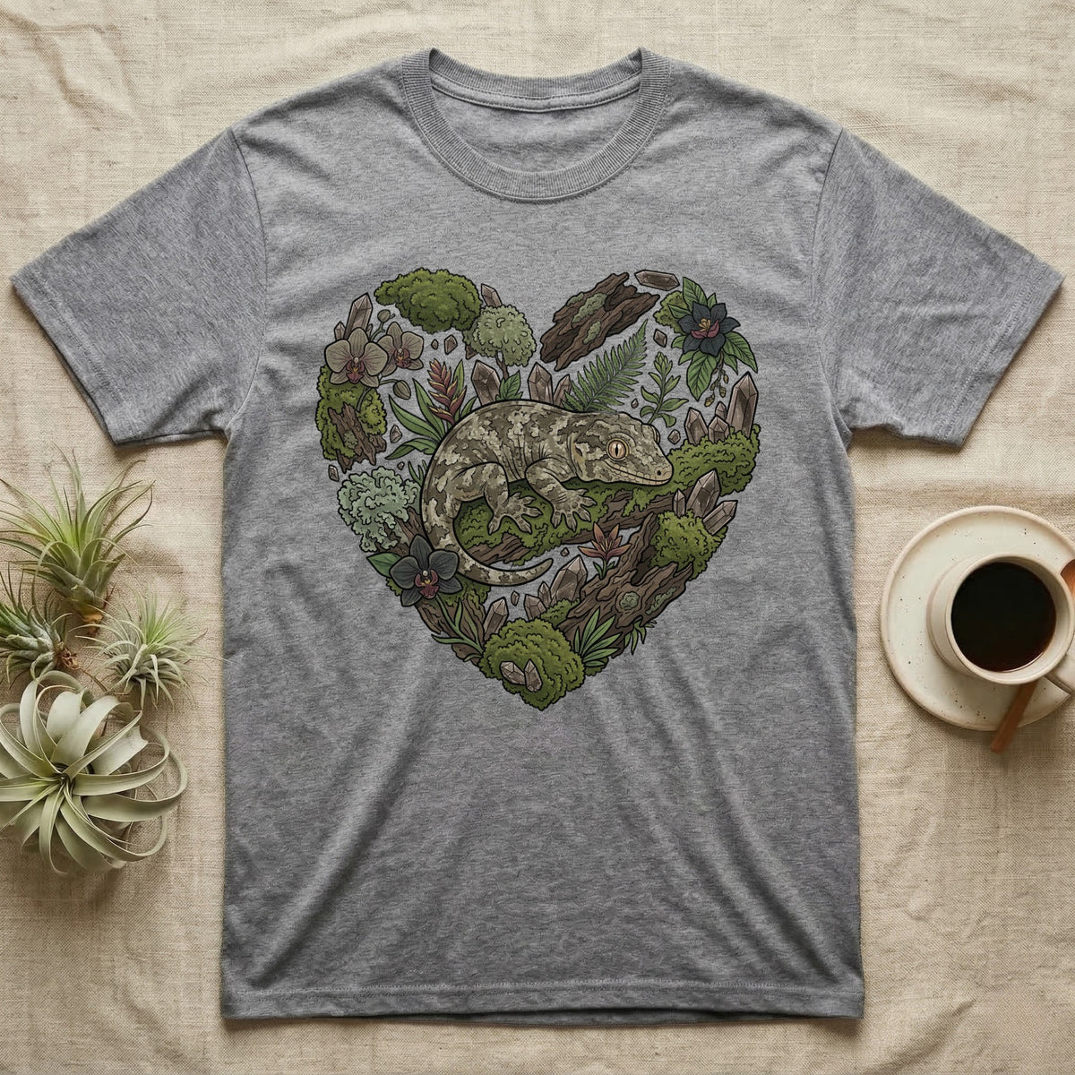Grey t-shirt with a heart-shaped design featuring a gecko among moss and foliage.