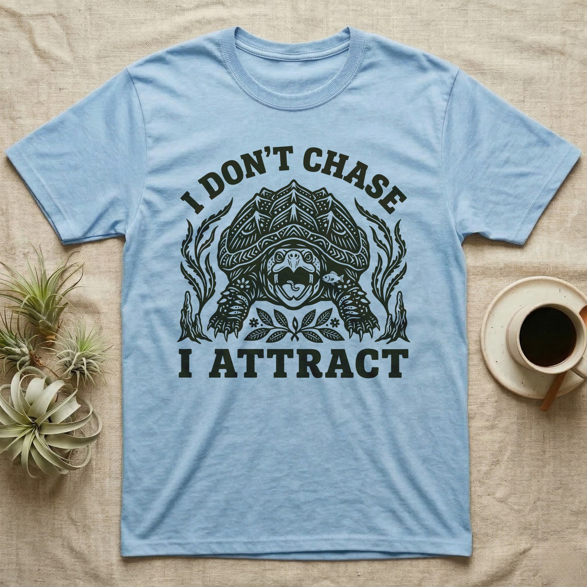 Alligator Snapper Lure T-Shirt in Light Blue — Folk-print alligator snapping turtle, jaws open, tongue lure out, a fish swimming in, text I Don't Chase I Attract