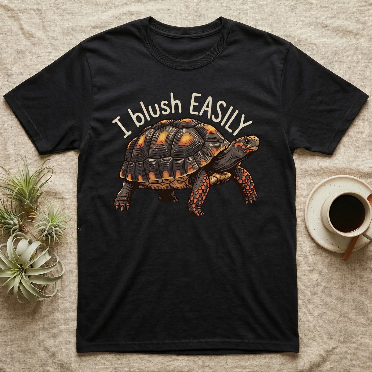 Red-Foot Tortoise Blush T-Shirt in Black — Red-footed tortoise with red-orange cheeks and legs walking under the curved words I blush EASILY