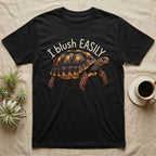 Red-Foot Tortoise Blush T-Shirt in Black — Red-footed tortoise with red-orange cheeks and legs walking under the curved words I blush EASILY