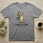 Bearded Dragon Salad Scam T-Shirt in Sport Grey — Storybook-cartoon bearded dragon holding wilted greens at arm's length and a tub of roaches, captioned "Salad Is a Scam".