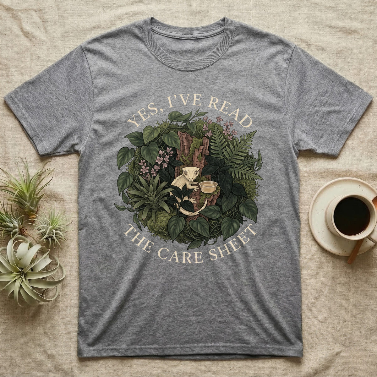 Crested Gecko Care Sheet T-Shirt in Sport Grey — Botanical wreath of pothos and moss circling a crested gecko, closed by two arcs of Roman capitals.