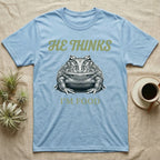 Pacman Frog He Thinks I'm Food T-Shirt in Light Blue — Engraved white-line illustration of a pacman frog staring straight ahead below retro script lettering reading HE THINKS.
