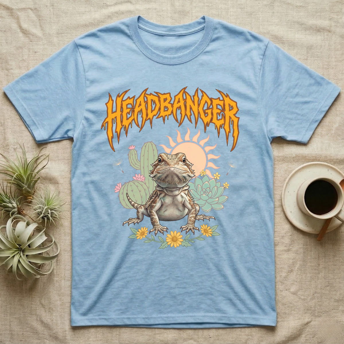 Central Bearded Dragon Feral T-Shirt in Light Blue — Baby bearded dragon in a pastel desert scene under a spiky amber metal wordmark reading HEADBANGER.