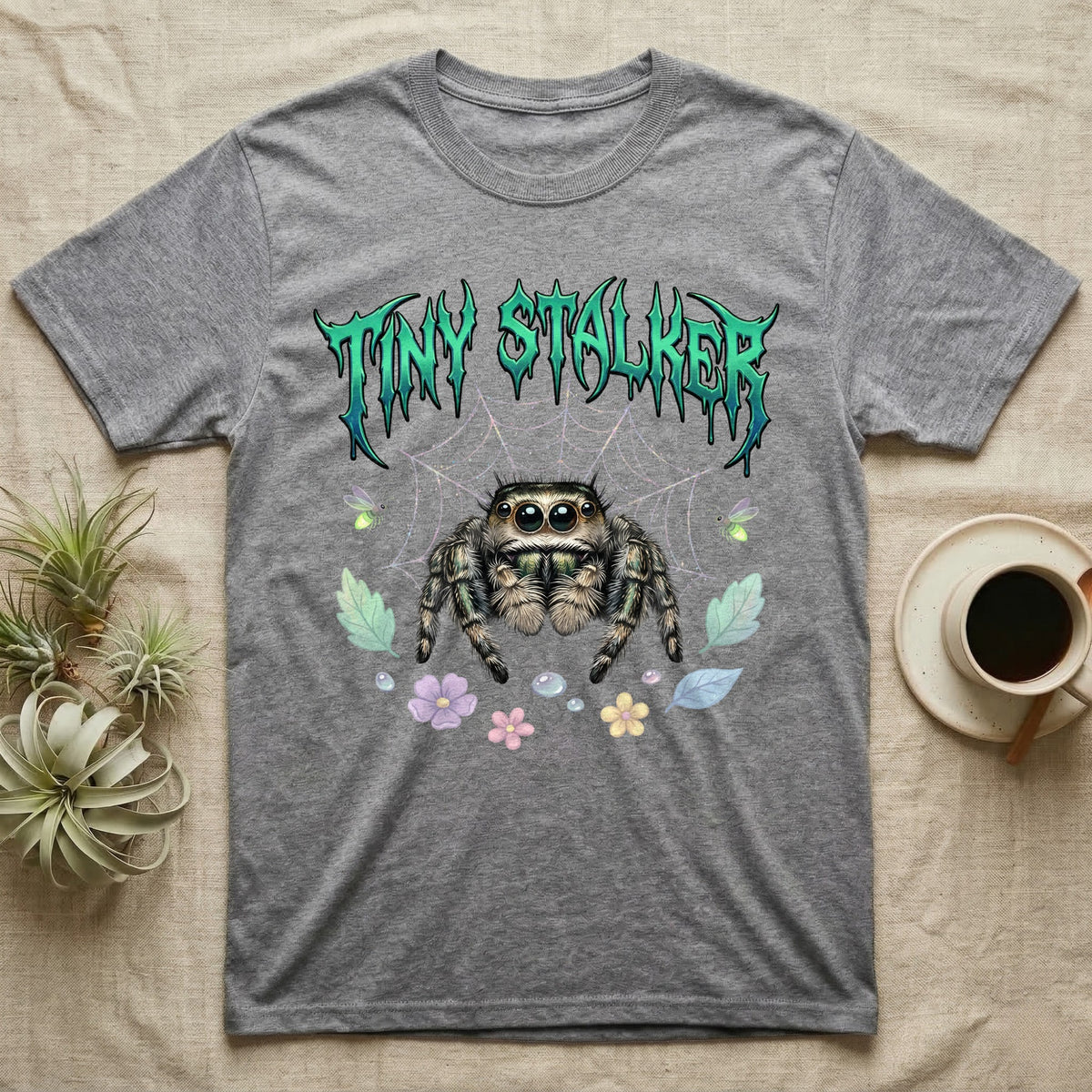 Regal Jumping Spider Feral T-Shirt in Sport Grey — Fuzzy jumping spider with huge eyes in a pastel garden under a spiky iridescent-teal metal wordmark reading TINY STALKER.