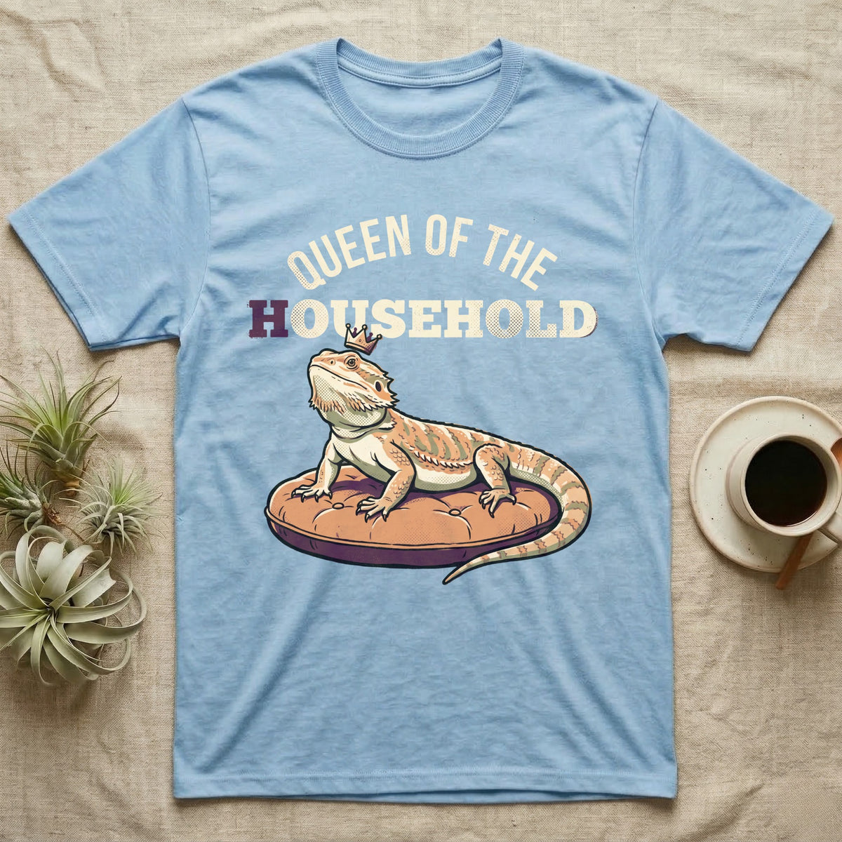Queen Bearded Dragon T-Shirt in Light Blue — Bold-vector illustration of a bearded dragon on a throne-cushion with a crown under varsity Queen of the Household lettering.