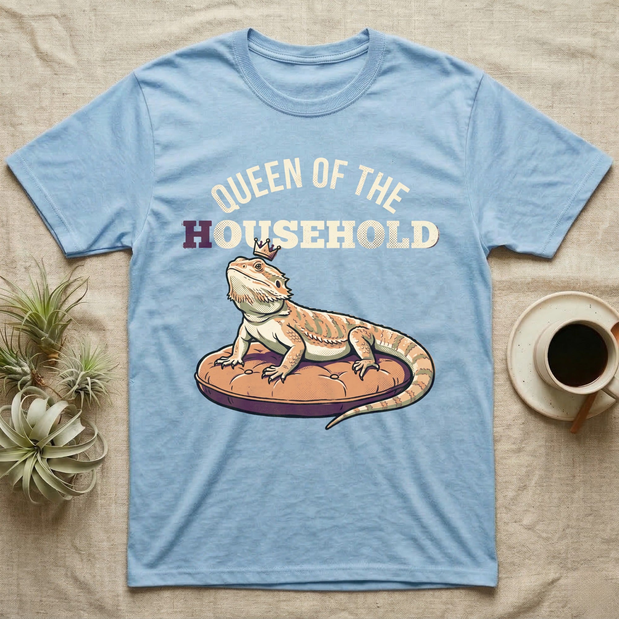 Queen Bearded Dragon T-Shirt in Light Blue — Bold-vector illustration of a bearded dragon on a throne-cushion with a crown under varsity Queen of the Household lettering.
