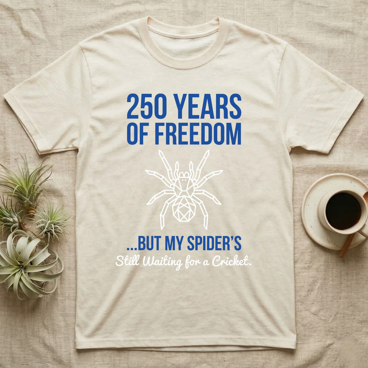 Tarantula Waiting For Cricket Tee in Natural — Minimalist geometric tee with a low-poly white tarantula and blue text reading 250 Years Of Freedom but my spider's still waiting for a cricket.