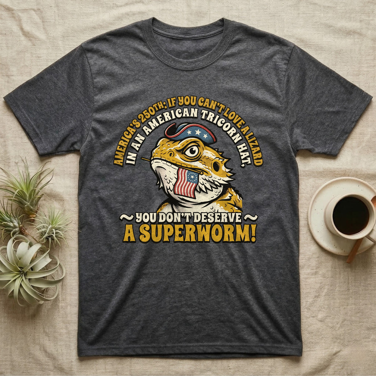 Bearded Dragon Tricorn Tee in Dark Heather — Bold woodcut tee of a bearded dragon in a colonial tricorn hat, gold and cream text reading You Don't Deserve A Superworm, on black.