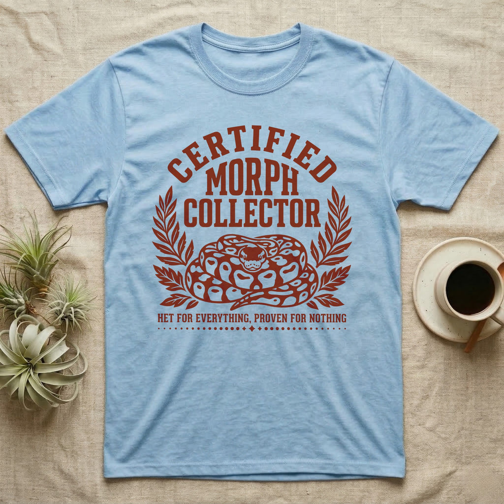 Ball Python Morph Crest T-Shirt in Light Blue — Linocut-style crest illustration of a coiled ball python with an arched "Certified Morph Collector" headline in rust ink.