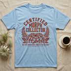 Ball Python Morph Crest T-Shirt in Light Blue — Linocut-style crest illustration of a coiled ball python with an arched "Certified Morph Collector" headline in rust ink.
