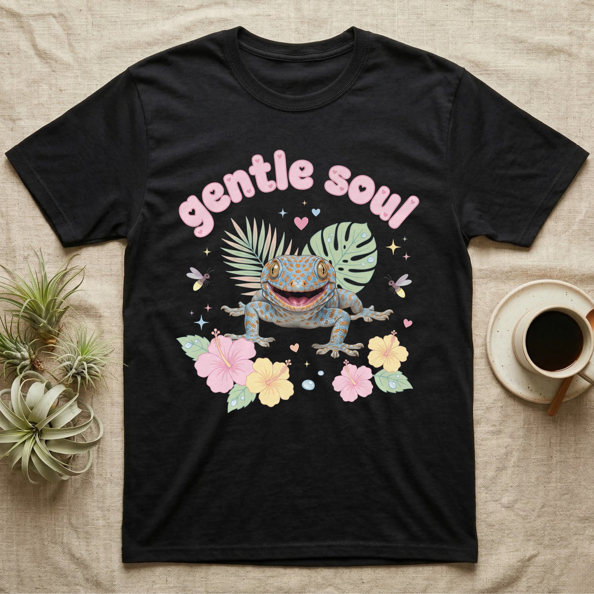 Tokay Gecko Baby T-Shirt in Black — Blue-and-orange spotted tokay gecko among pastel leaves and hibiscus under puffy pink bubble text "gentle soul".