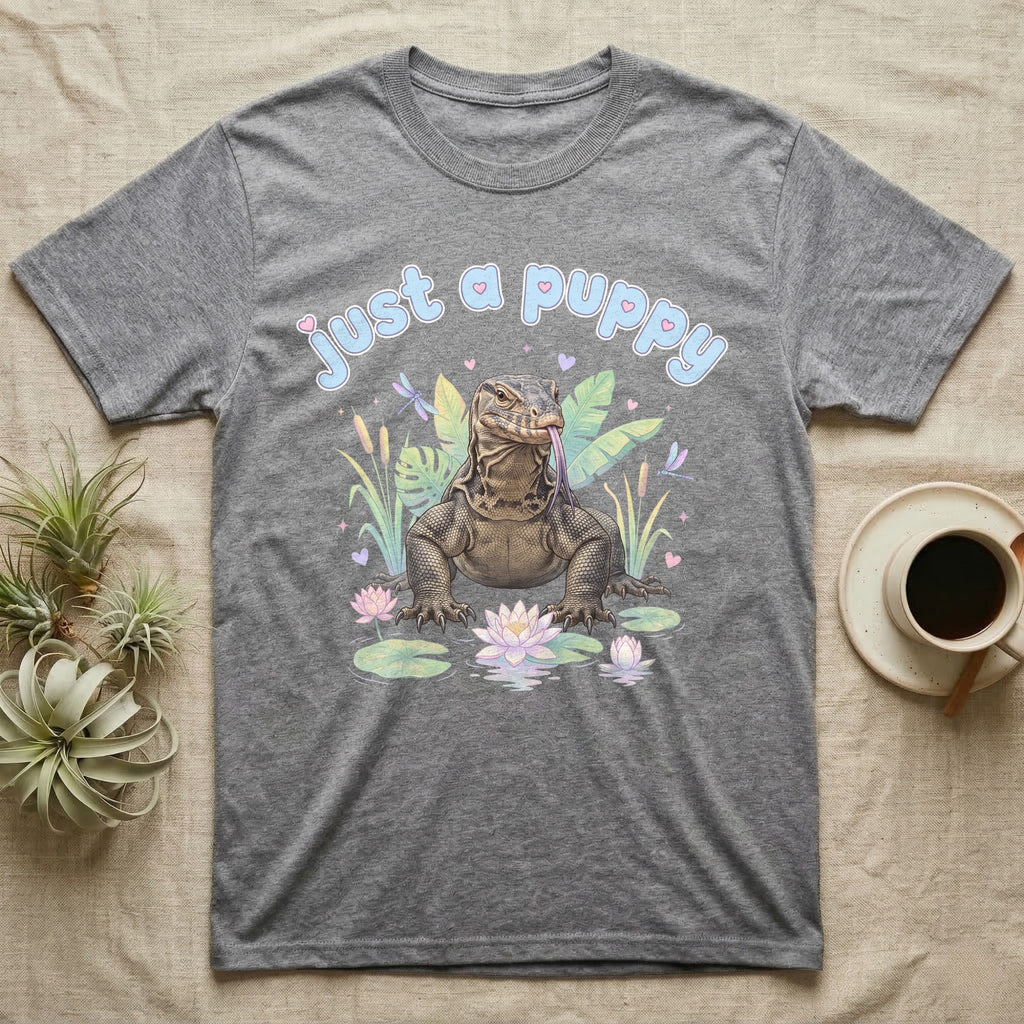 Asian Water Monitor Baby T-Shirt in Sport Grey — Asian water monitor with tongue out among pastel reeds and lotus under puffy blue bubble text "just a puppy".