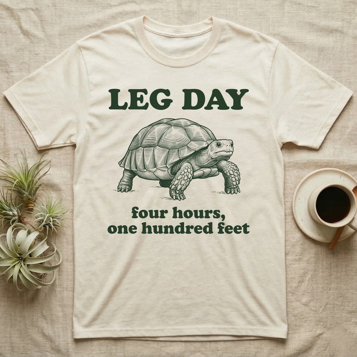 Sulcata Tortoise Leg Day T-Shirt in Natural — Engraved sulcata tortoise in deep green ink beneath the words LEG DAY, with four hours, one hundred feet below.