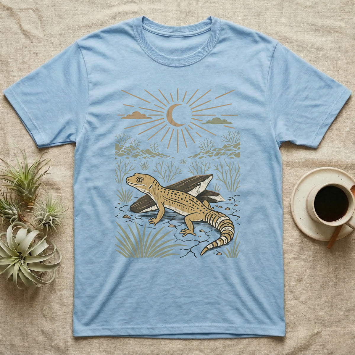 Leopard Gecko Home Range T-Shirt in Light Blue — Woodcut-style illustration of a leopard gecko standing on cracked earth beside flat stones with thorn scrub behind, no on-shirt text.