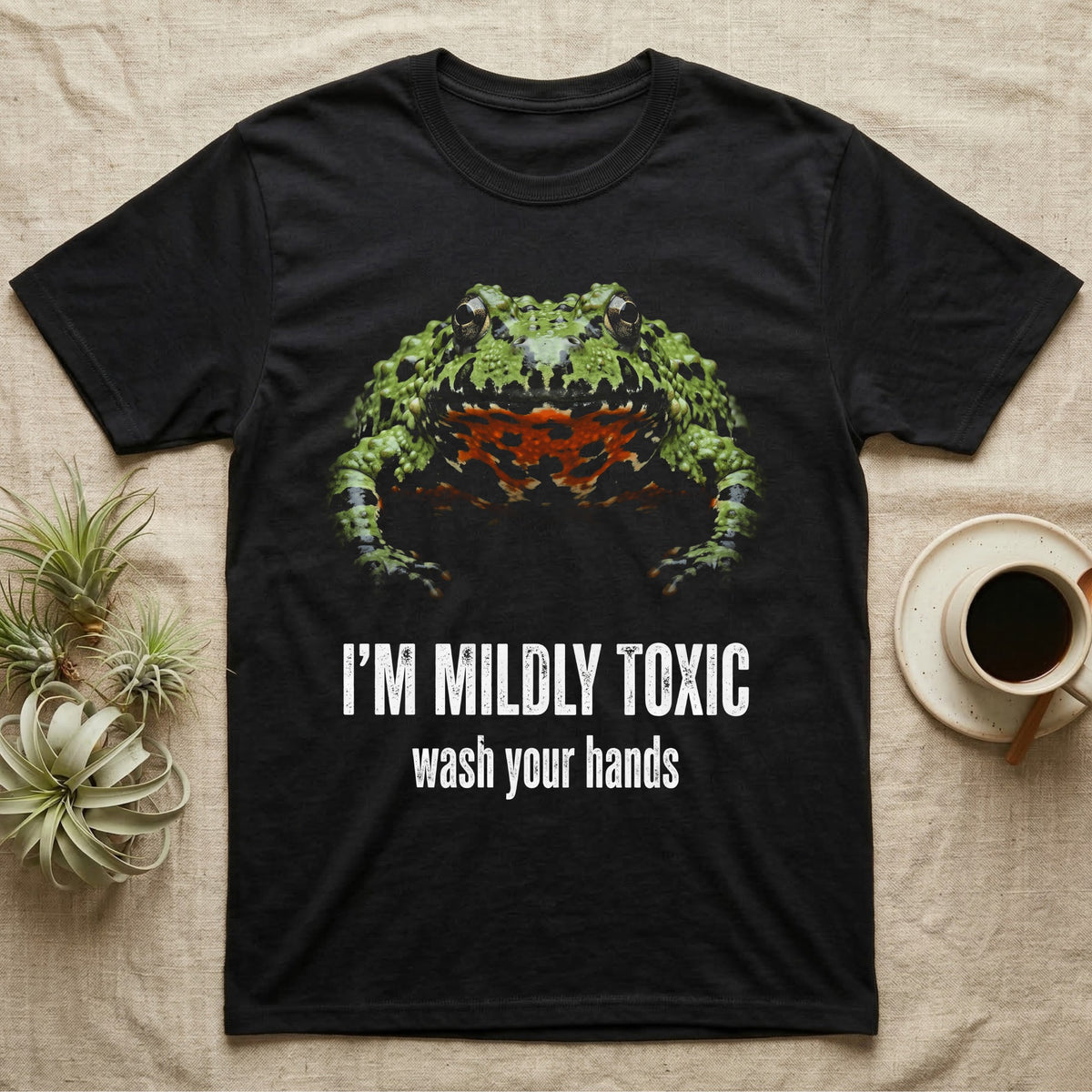 Deadpan mugshot of an olive-green fire-bellied toad on black, captioned I'm mildly toxic, wash your hands. — shown on a Black tee.