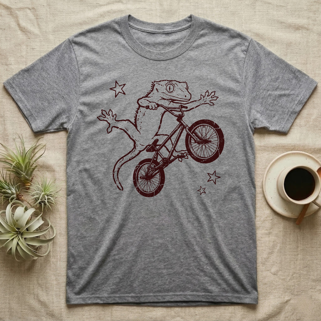 Crested Gecko BMX T-Shirt in Sport Grey — Distressed one-ink oxblood screenprint of a crested gecko airborne on a BMX bike mid-barspin, front hands thrown wide, back feet gripping the pedals.