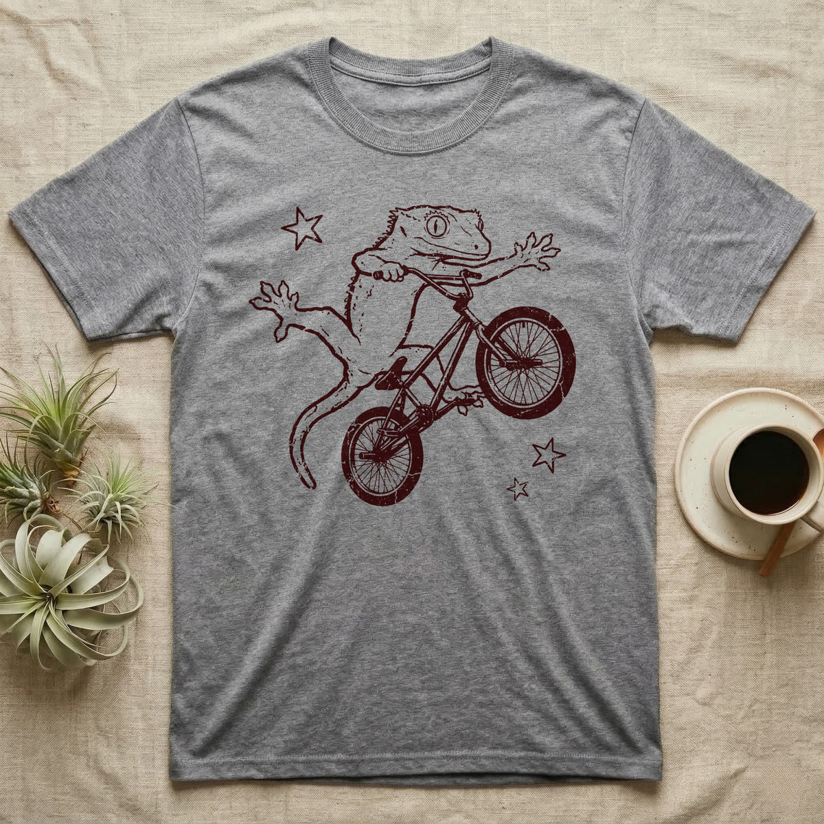 Crested Gecko BMX T-Shirt in Sport Grey — Distressed one-ink oxblood screenprint of a crested gecko airborne on a BMX bike mid-barspin, front hands thrown wide, back feet gripping the pedals.