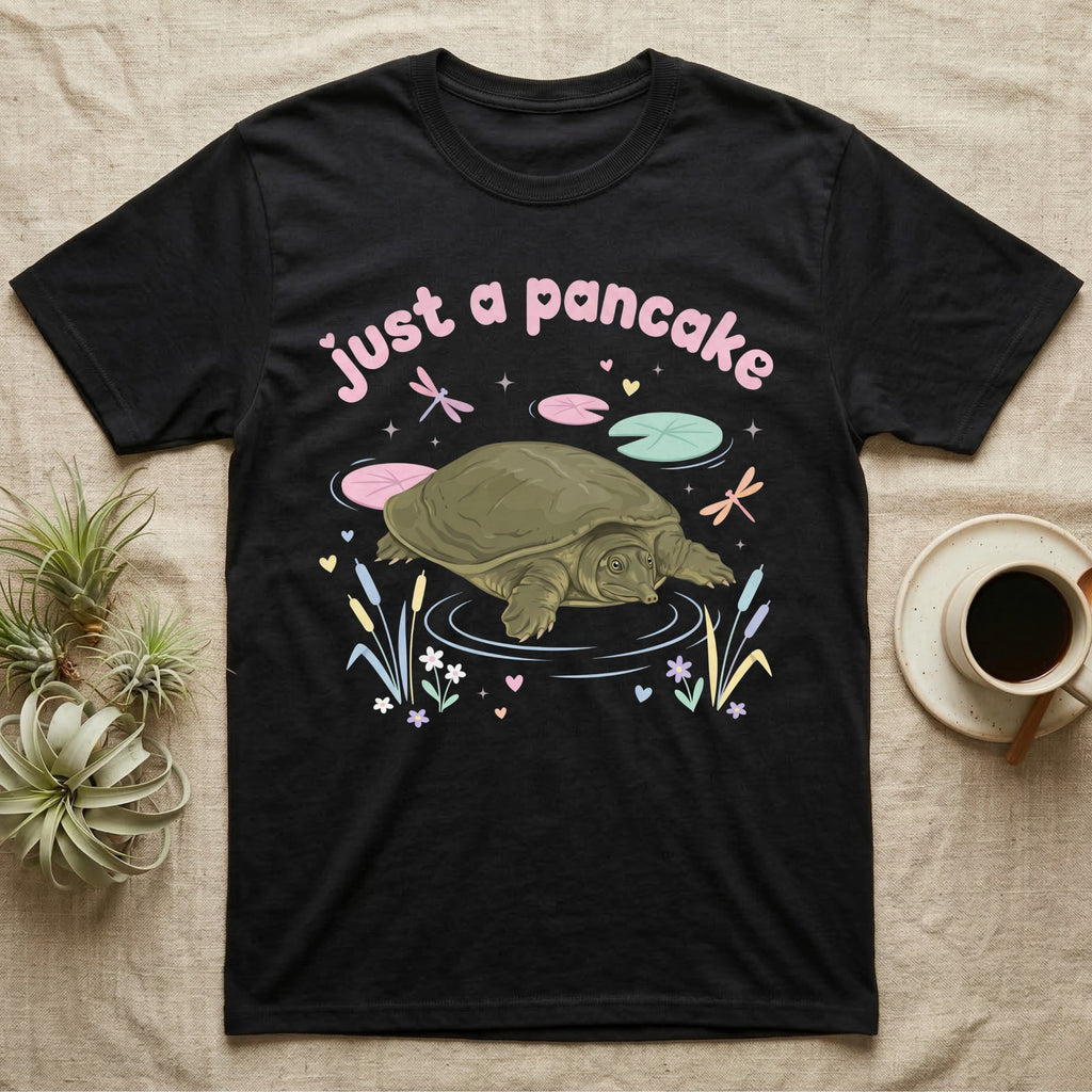 Spiny Softshell Turtle Baby T-Shirt in Black — Pastel spiny softshell turtle with flat shell and snorkel nose among lily pads, puffy pink wordmark "just a pancake" above.