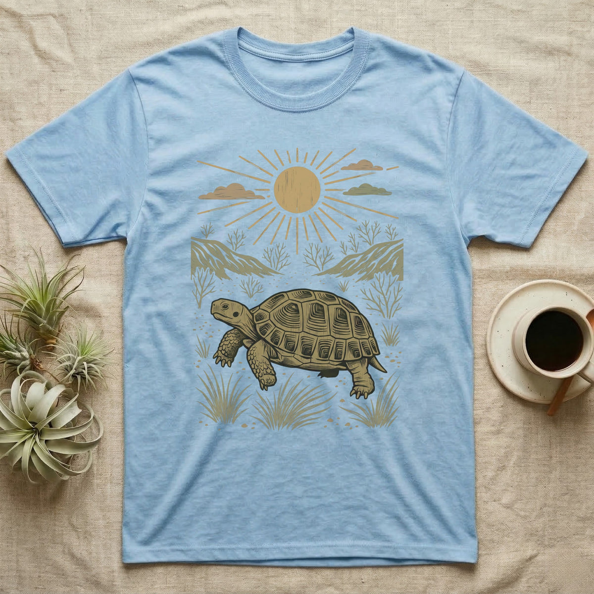 Russian Tortoise Home Range T-Shirt in Light Blue — Woodcut-style illustration of a Russian tortoise walking across gravelly steppe under a full sun with dry hills behind, no on-shirt text.
