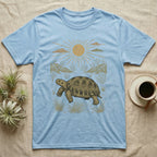 Russian Tortoise Home Range T-Shirt in Light Blue — Woodcut-style illustration of a Russian tortoise walking across gravelly steppe under a full sun with dry hills behind, no on-shirt text.