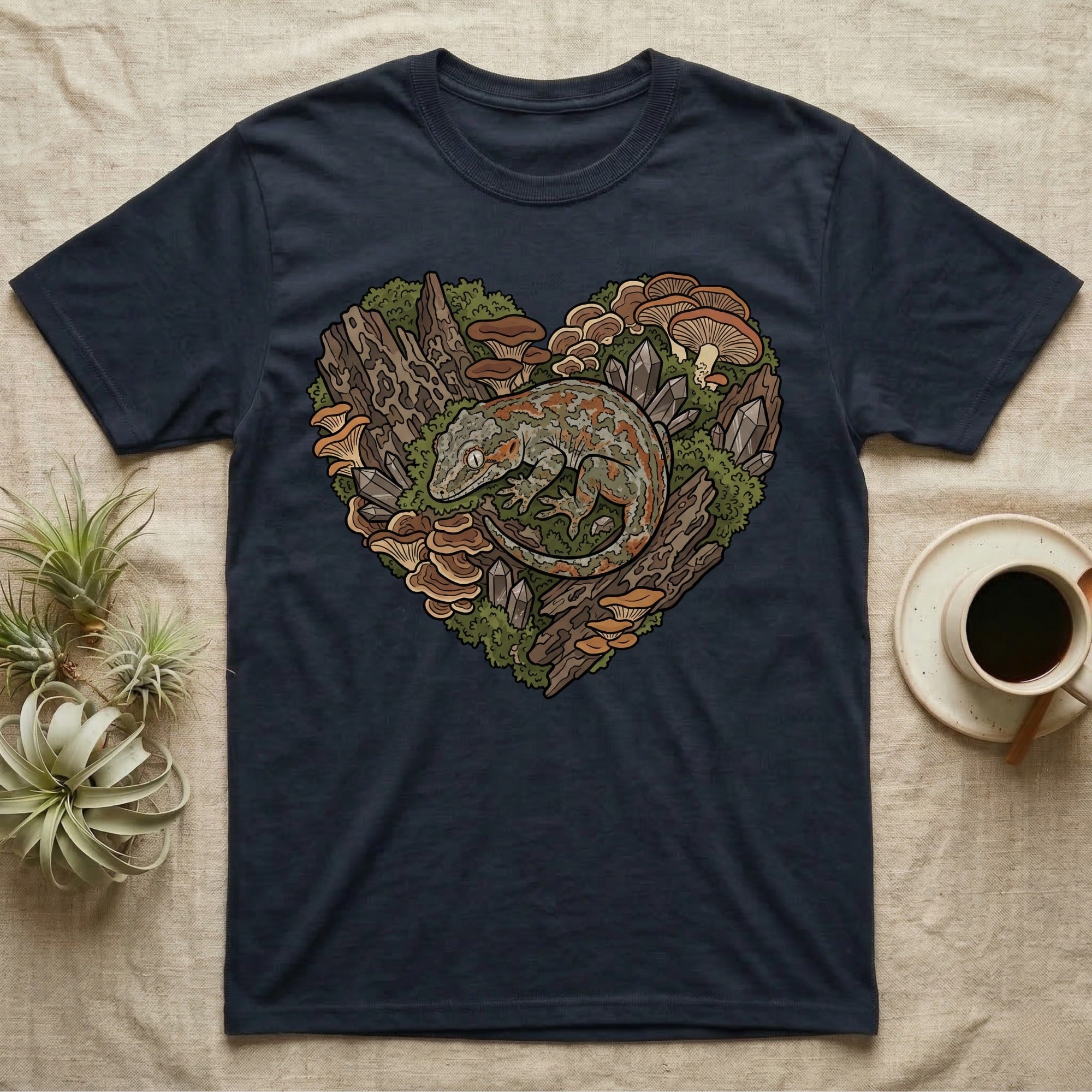 Navy t-shirt featuring a gecko nestled in moss, mushrooms, and crystals forming a heart.