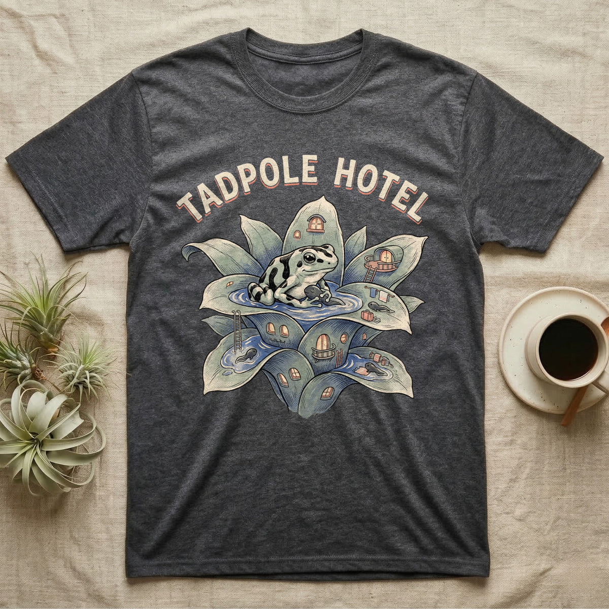 Tadpole Hotel Frog T-Shirt in Dark Heather — Whimsical naturalist illustration of a dart frog tucking tadpoles into a bromeliad Tadpole Hotel with hand-lettered marquee text.