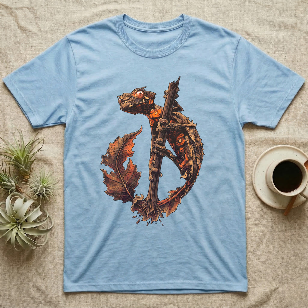 Vintage ink illustration of an eyelash leaf-tailed gecko clinging to a branch with its tail curled beside a serrated leaf, no on-shirt text. — shown on a Light Blue tee.