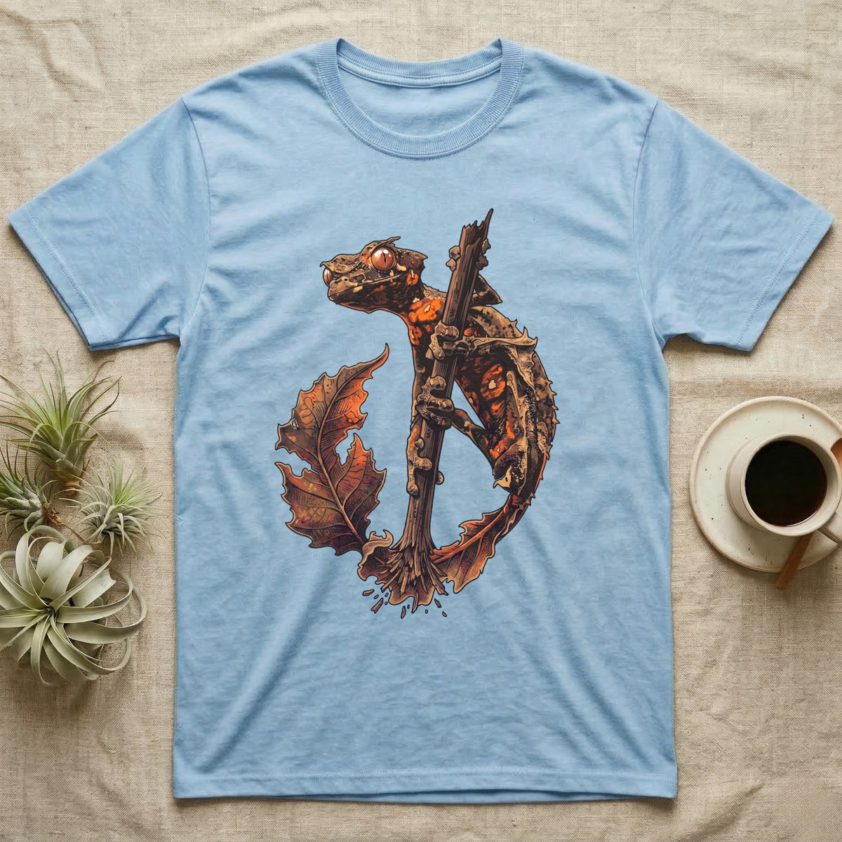 Vintage ink illustration of an eyelash leaf-tailed gecko clinging to a branch with its tail curled beside a serrated leaf, no on-shirt text. — shown on a Light Blue tee.
