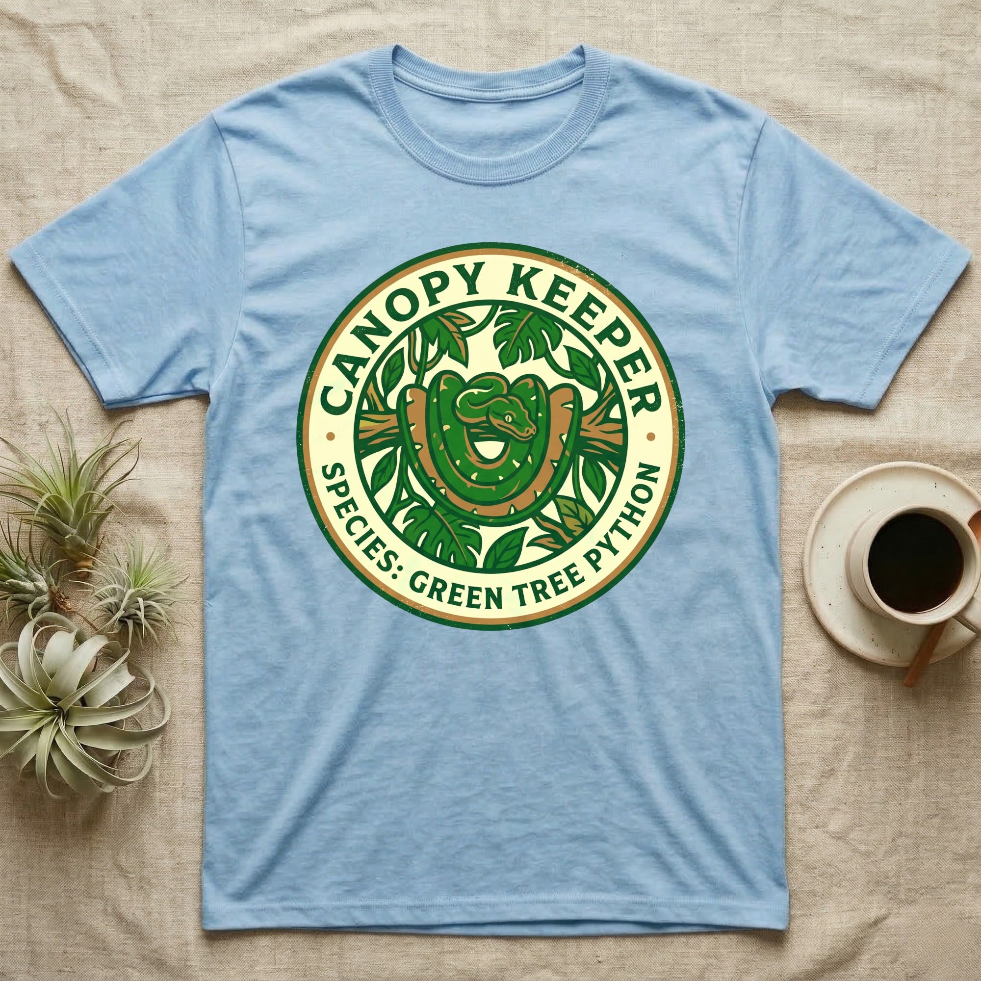 Light blue t-shirt with green circular "Canopy Keeper Species: Green Tree Python" logo.