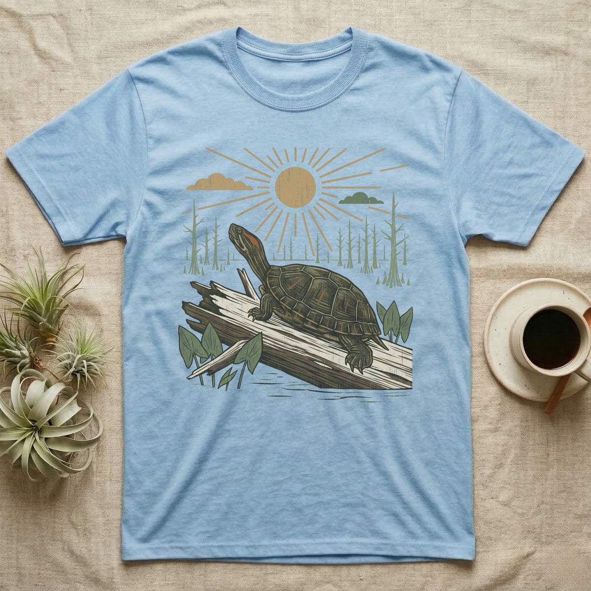 Red-Eared Slider Home Range T-Shirt in Light Blue — Woodcut-style illustration of a red-eared slider basking on a half-sunk log in a cypress swamp under a full sun, no on-shirt text.