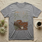 Corn Snake Home Range T-Shirt in Sport Grey — Woodcut-style illustration of a corn snake winding across pine straw beside a split log with pine trees behind, no on-shirt text.