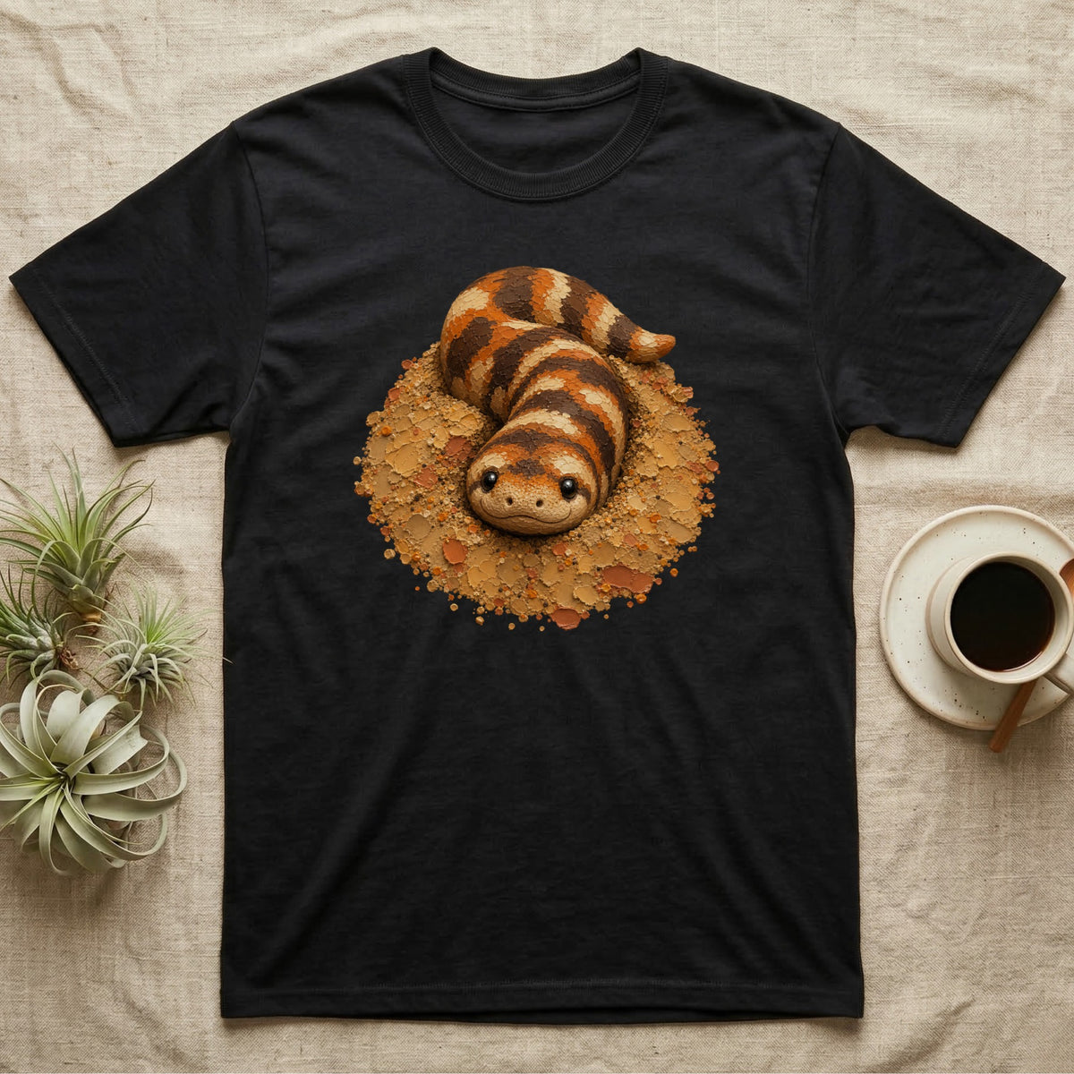 Black t-shirt with illustration of a cute, striped desert snake in a sandy nest.