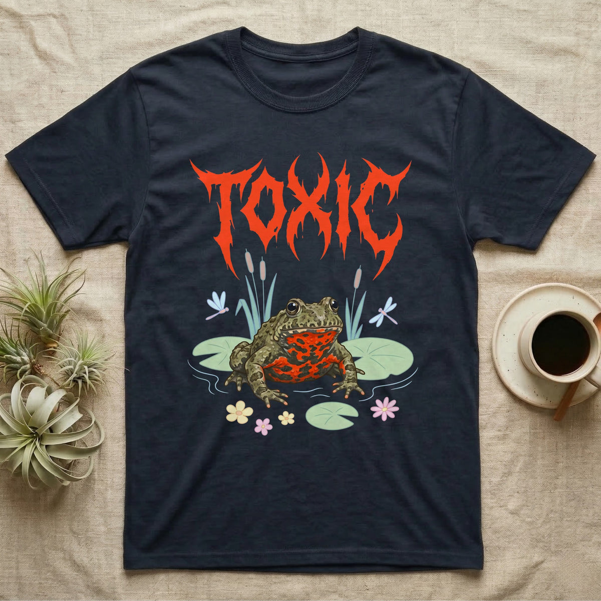 Oriental Fire-Bellied Toad Feral T-Shirt in Navy — Pastel fire-bellied toad with red-orange belly among lily pads and dragonflies, jagged metal wordmark "TOXIC" above.