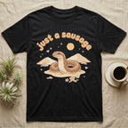 Kenyan Sand Boa Softie T-Shirt in Black — Kenyan sand boa looping out of pastel sand dunes under a puffy "just a sausage" bubble wordmark with tiny hearts.
