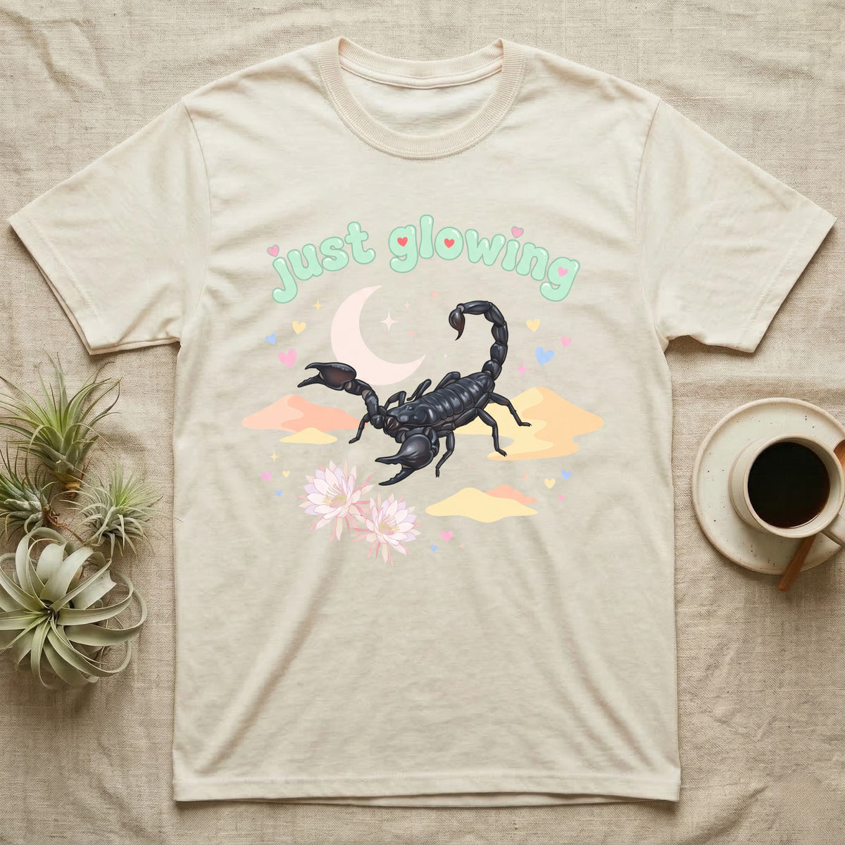 Emperor Scorpion Baby T-Shirt in Natural — Black emperor scorpion, pincers raised, under a pastel moon and stars with puffy mint bubble text "just glowing".