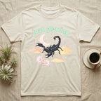Emperor Scorpion Baby T-Shirt in Natural — Black emperor scorpion, pincers raised, under a pastel moon and stars with puffy mint bubble text "just glowing".