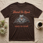 Glass Frog Engraving T-Shirt in Dark Chocolate — White-line engraving of a glass frog sitting on a leaf with a coral heart showing through its belly, between Hard To Spot and easy to read