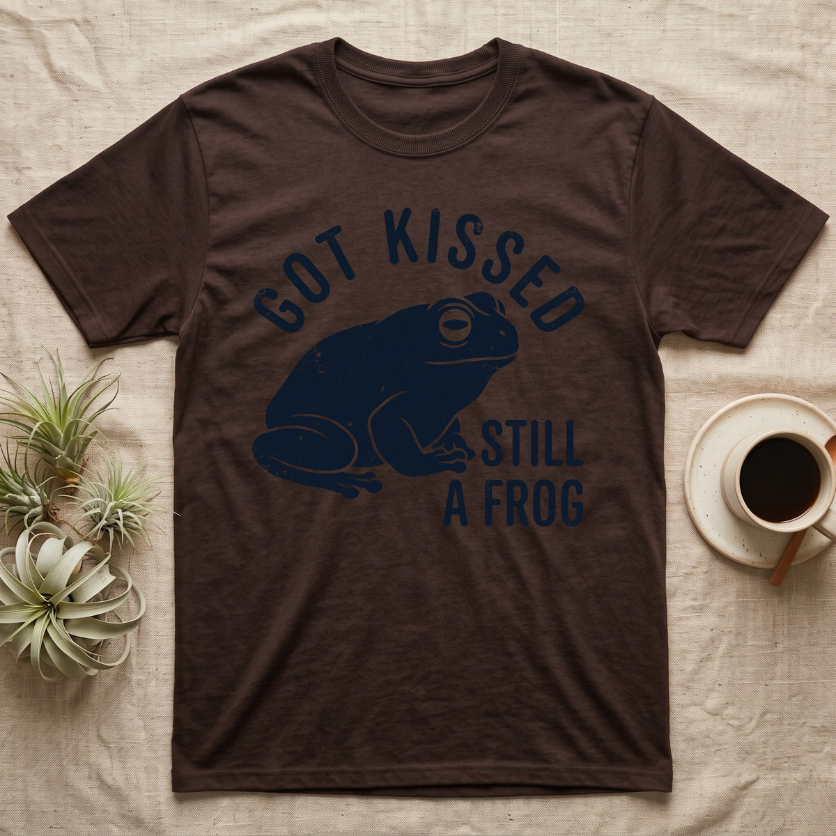 Tree Frog Kissed T-Shirt in Dark Chocolate — Worn navy silhouette of a dumpy White's tree frog under the words Got Kissed Still A Frog