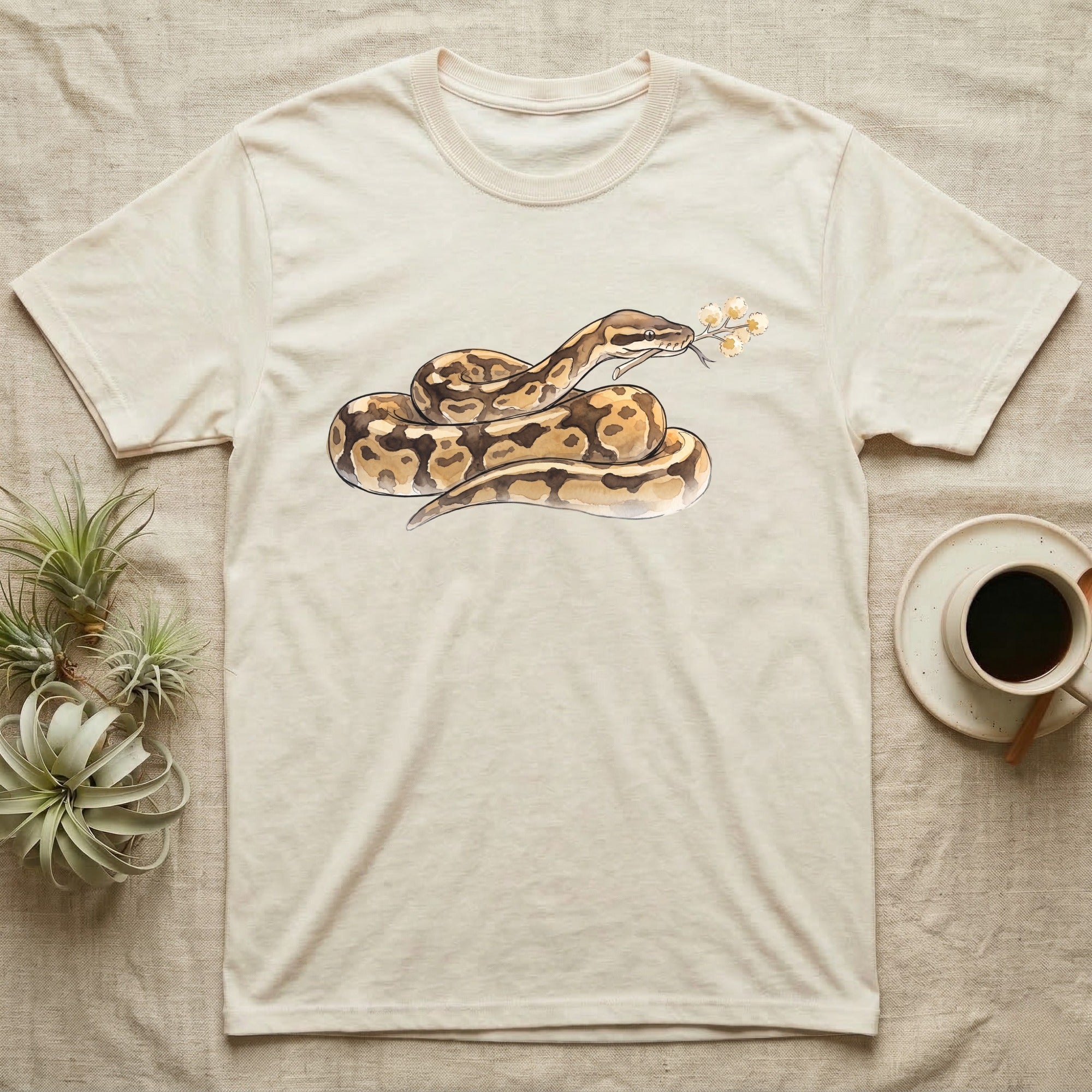 Ball Python Blossom T-Shirt in Natural — Watercolor illustration of a tan-and-brown ball python holding an acacia blossom sprig, on a dark grey t-shirt.