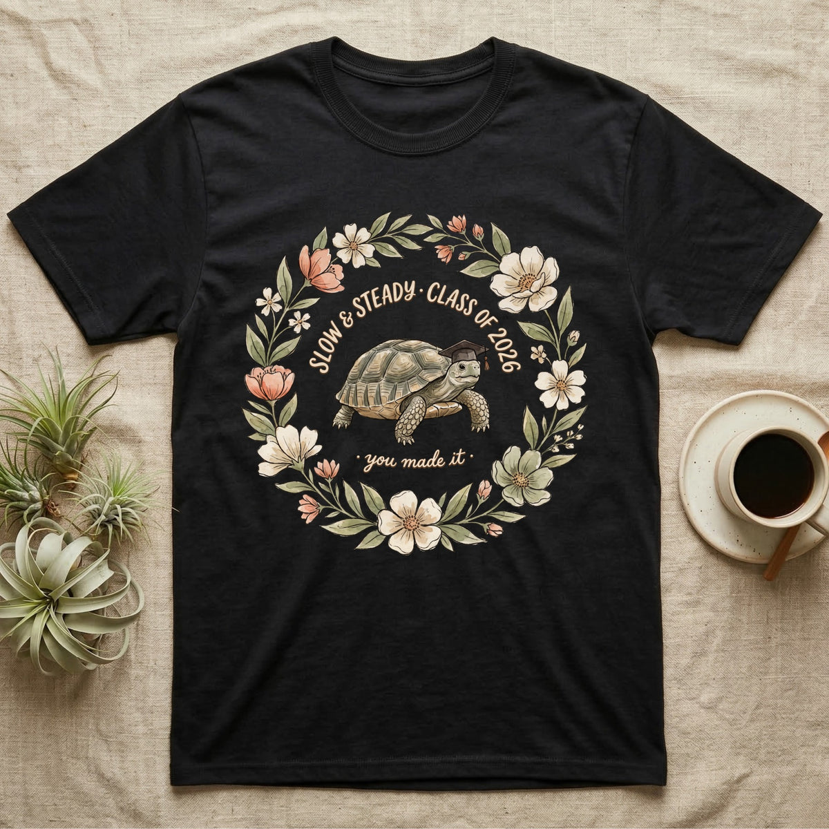 Slow And Steady Graduation T-Shirt in Black — Watercolour illustration of a tortoise in a graduation cap inside a floral wreath with "Slow & Steady, Class of 2026."