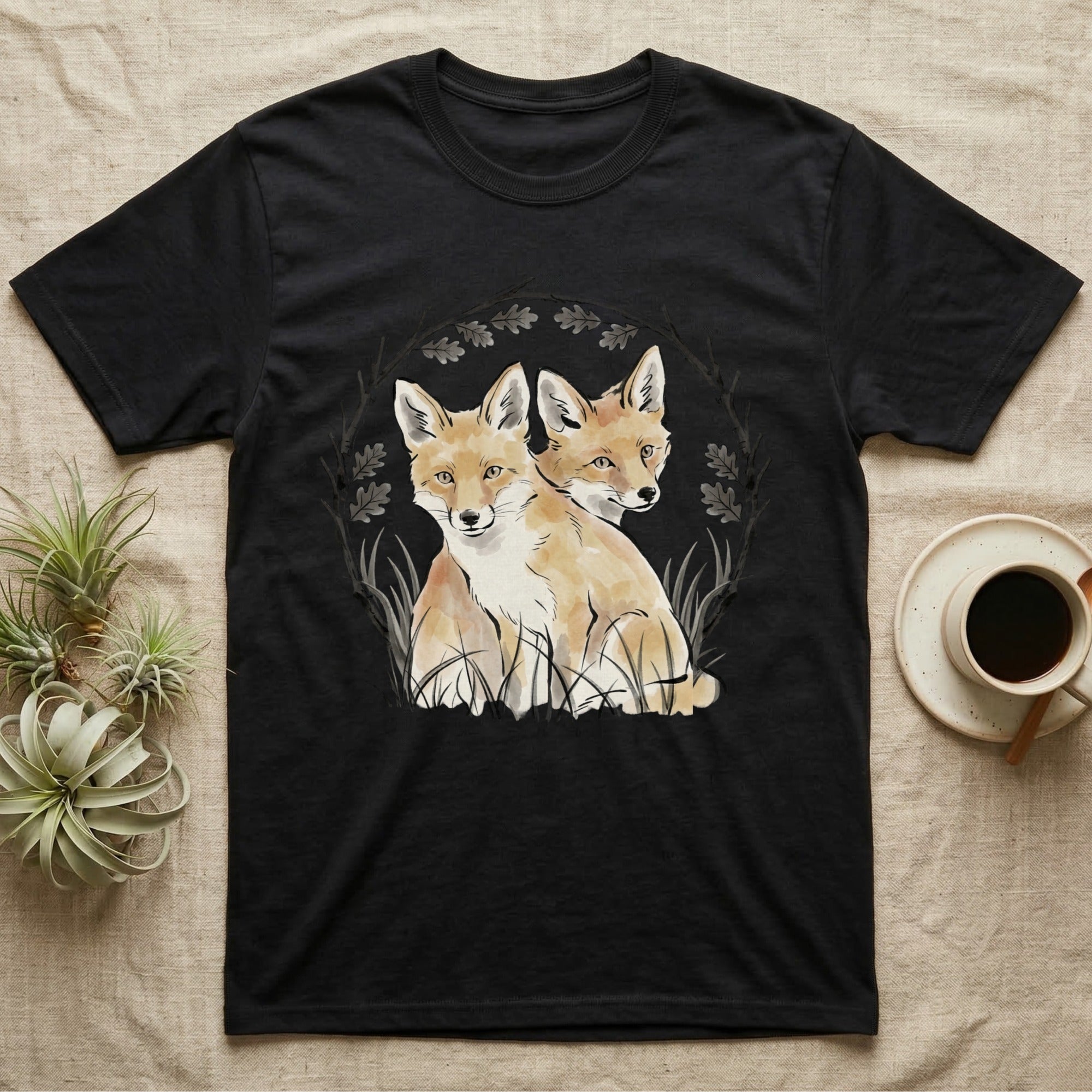 Black t-shirt with watercolor illustration of two foxes framed by leaves and branches.