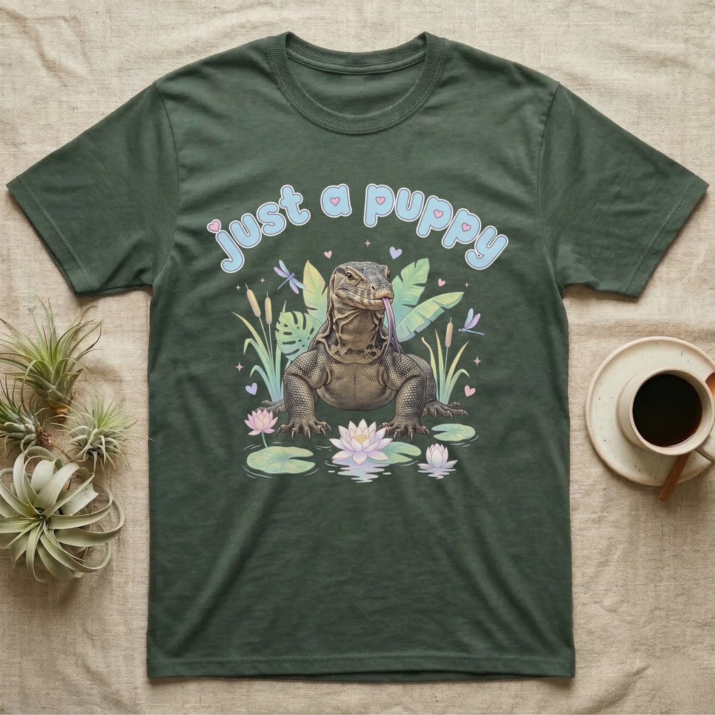 Asian Water Monitor Baby T-Shirt in Military Green — Asian water monitor with tongue out among pastel reeds and lotus under puffy blue bubble text "just a puppy".